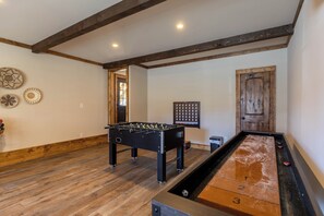 A room with a foosball table, shuffleboard table, wooden flooring, and a door with a wooden frame. - Casa Tres Cuervos at Eagles Nest (Banner Elk)
