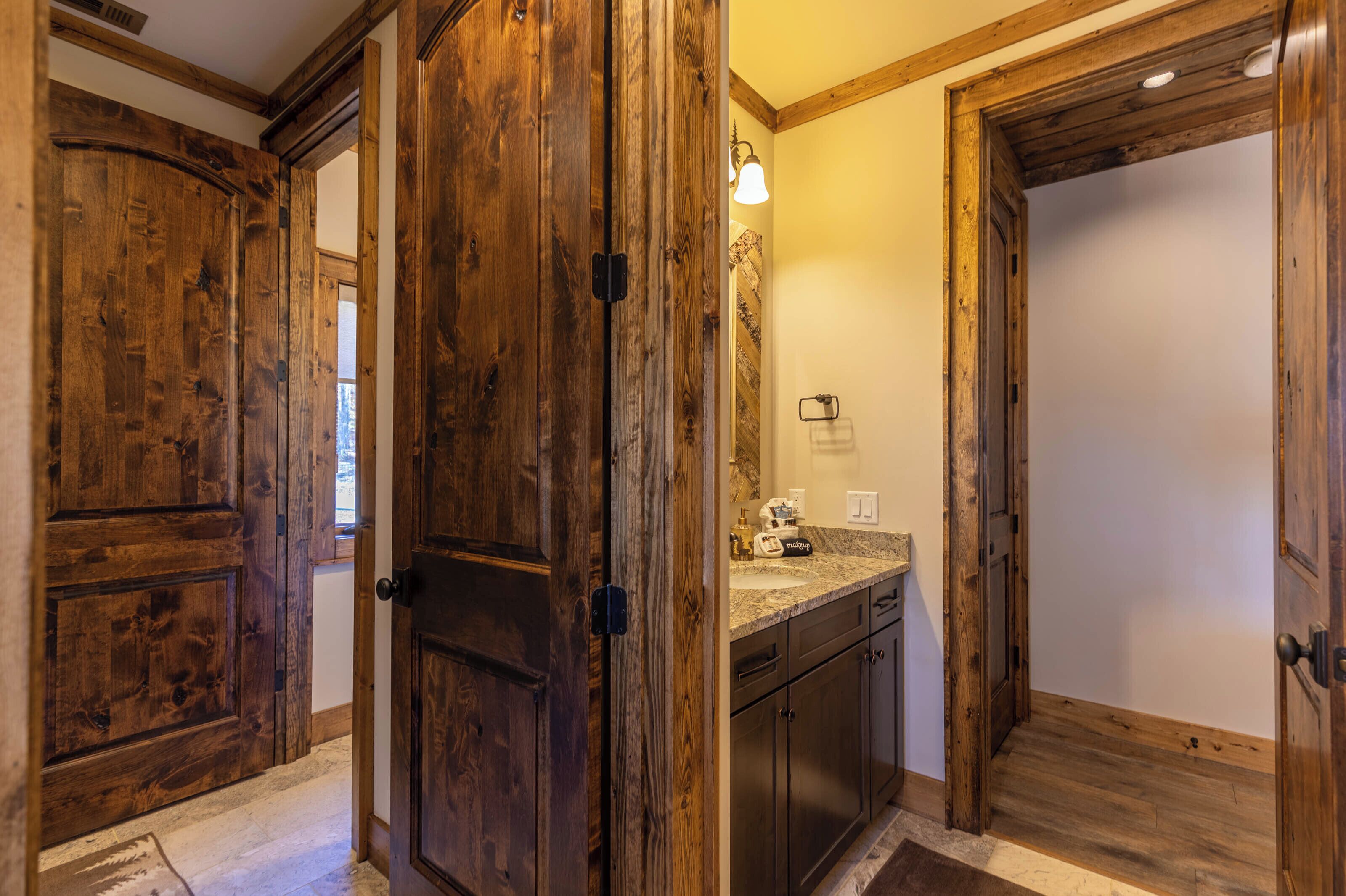 A wooden door leading to a bathroom with a sink and mirror.