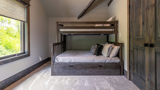 A bunk bed with a storage drawer, a window with a view of greenery, and a wooden door. - Just Bluffin' at Eagles Nest (Banner Elk)