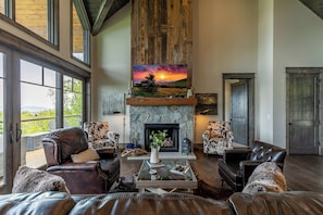 A spacious living room with leather sofas, a fireplace, and a large painting of a sunset. - Just Bluffin' at Eagles Nest (Banner Elk)