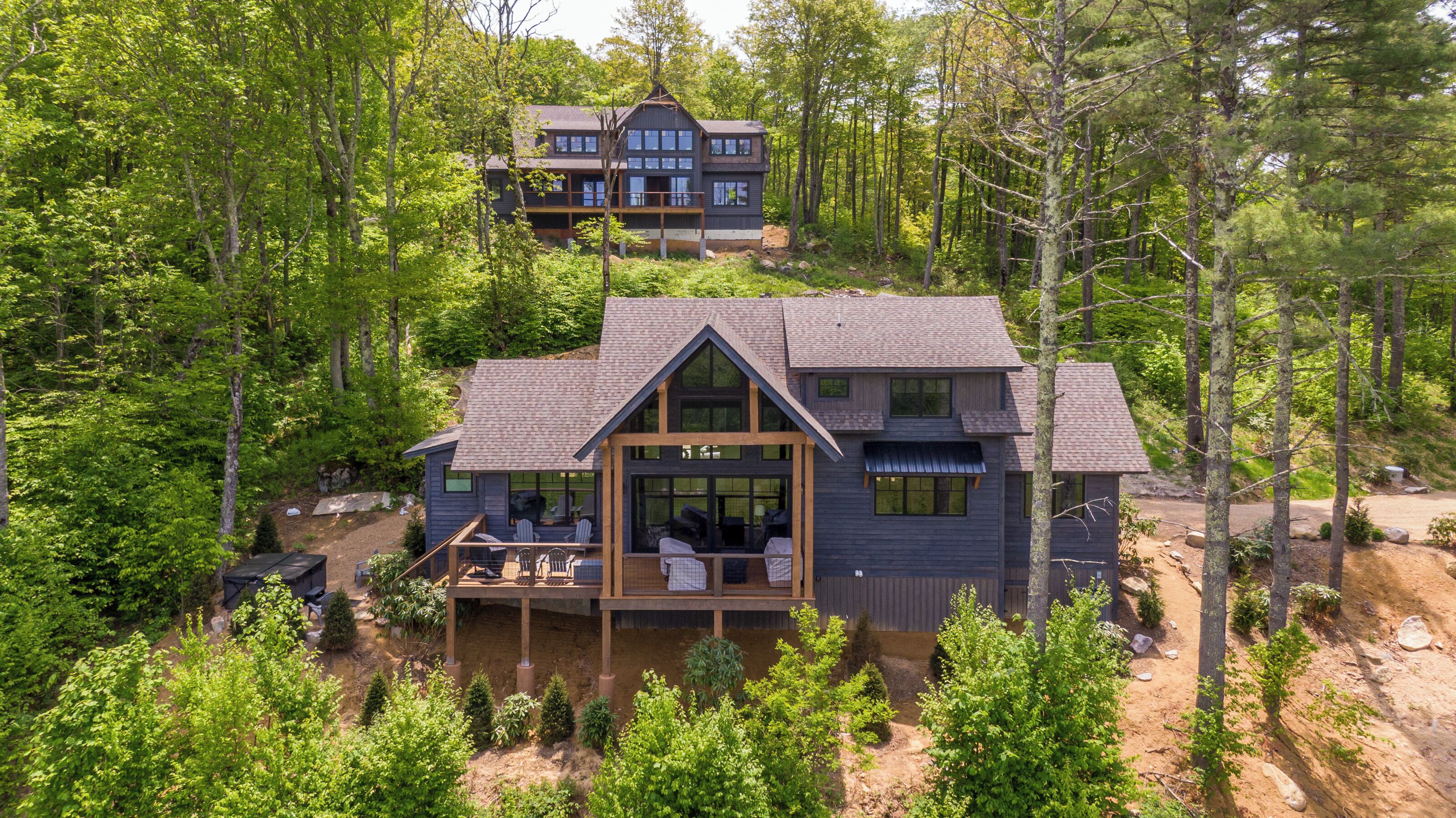 A two-story cabin with a deck, surrounded by dense forest.