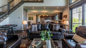 A spacious living room with a leather sofa, a coffee table with magazines, and a staircase leading to an upper level. - Just Bluffin' at Eagles Nest (Banner Elk)