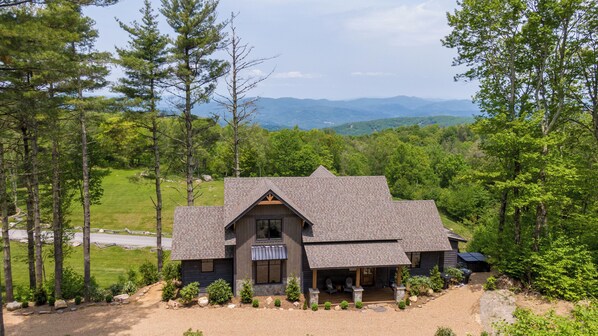 A cabin with a sloped roof, surrounded by trees and a view of distant mountains. - Just Bluffin' at Eagles Nest (Banner Elk)