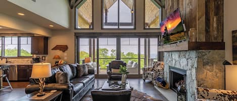 Amplia sala de estar con chimenea, muebles de cuero y grandes ventanales con vistas al exterior.