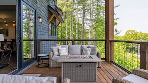 A covered deck with a fire pit, outdoor seating, and a view of a forest. - Just Bluffin' at Eagles Nest (Banner Elk)