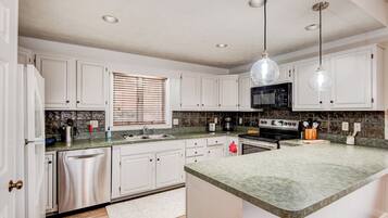 A modern kitchen with white cabinets, granite countertops, a stainless steel refrigerator, a built-in oven, and a microwave.
