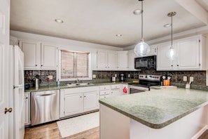 A modern kitchen with white cabinets, granite countertops, a stainless steel refrigerator, a built-in oven, and a microwave. - Chetola Robin 1 (Blowing Rock)