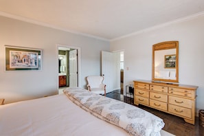 A bedroom with a large bed, a wooden dresser, a chair, and a mirror.