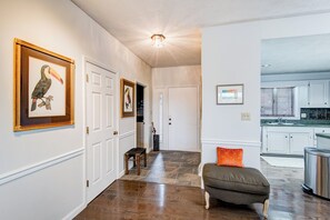 A hallway with framed artwork, a bench, and a kitchen area visible through an open door.