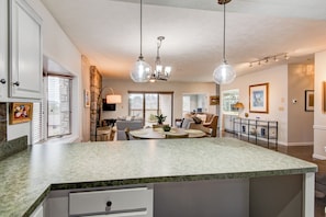 A spacious kitchen with a large island, pendant lights, and a dining area with a sofa and chairs.