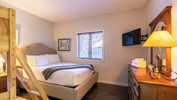 A bedroom with a bed, a window with blinds, a bedside table with a lamp, and a dresser.