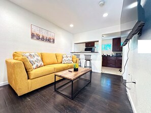 Ein Wohnzimmer mit einer Couch, einem Couchtisch und einer Küche im Hintergrund.