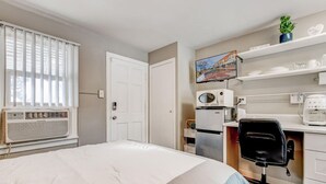 Ein Schlafzimmer mit Bett, Schreibtisch mit Stuhl, einer Mikrowelle, einem Kühlschrank und einem Fernseher.