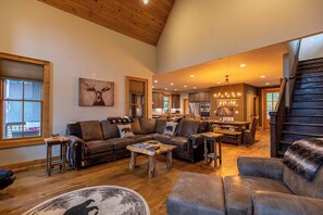 A spacious living room with a large sectional sofa, a coffee table, and a fireplace. There is a kitchen area with modern appliances and a dining table. - Bearingers Bluff at Eagles Nest (Banner Elk)