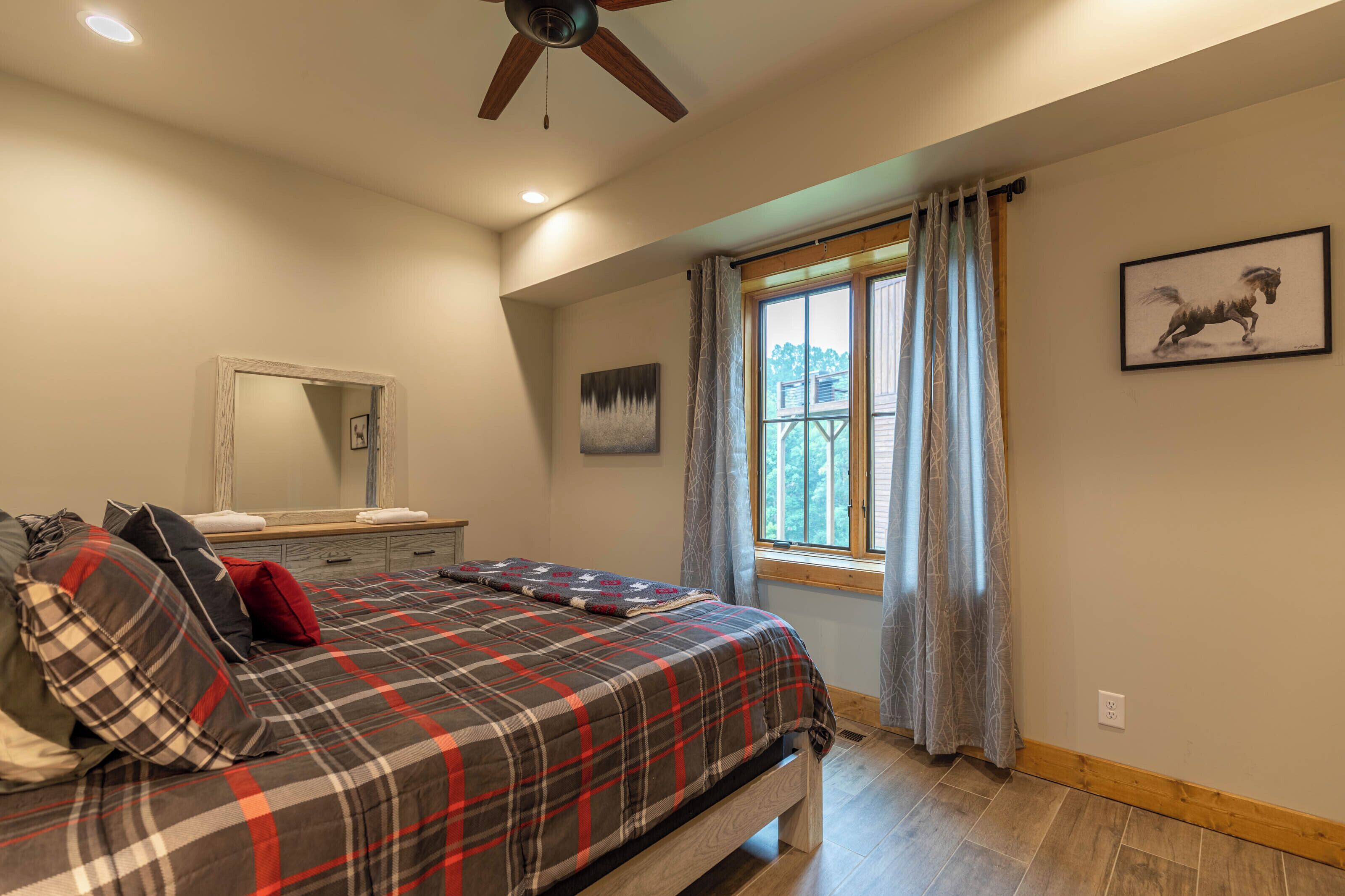 Ein Schlafzimmer mit Bett, Deckenventilator, Fenster mit Vorhängen und einem Gemälde an der Wand.