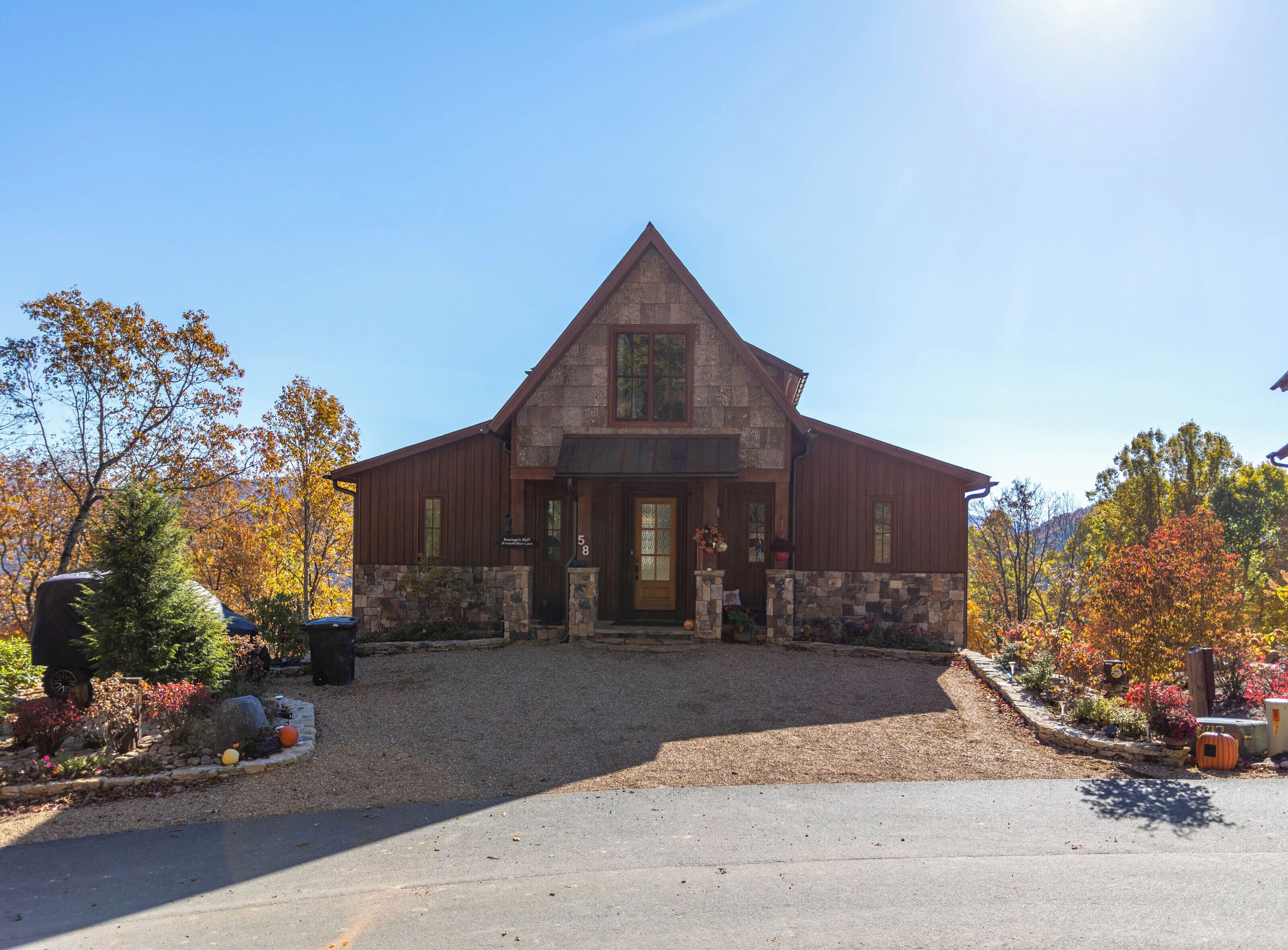 A two-story stone building with a steep gable roof, a front porch, and a driveway leading to the entrance.