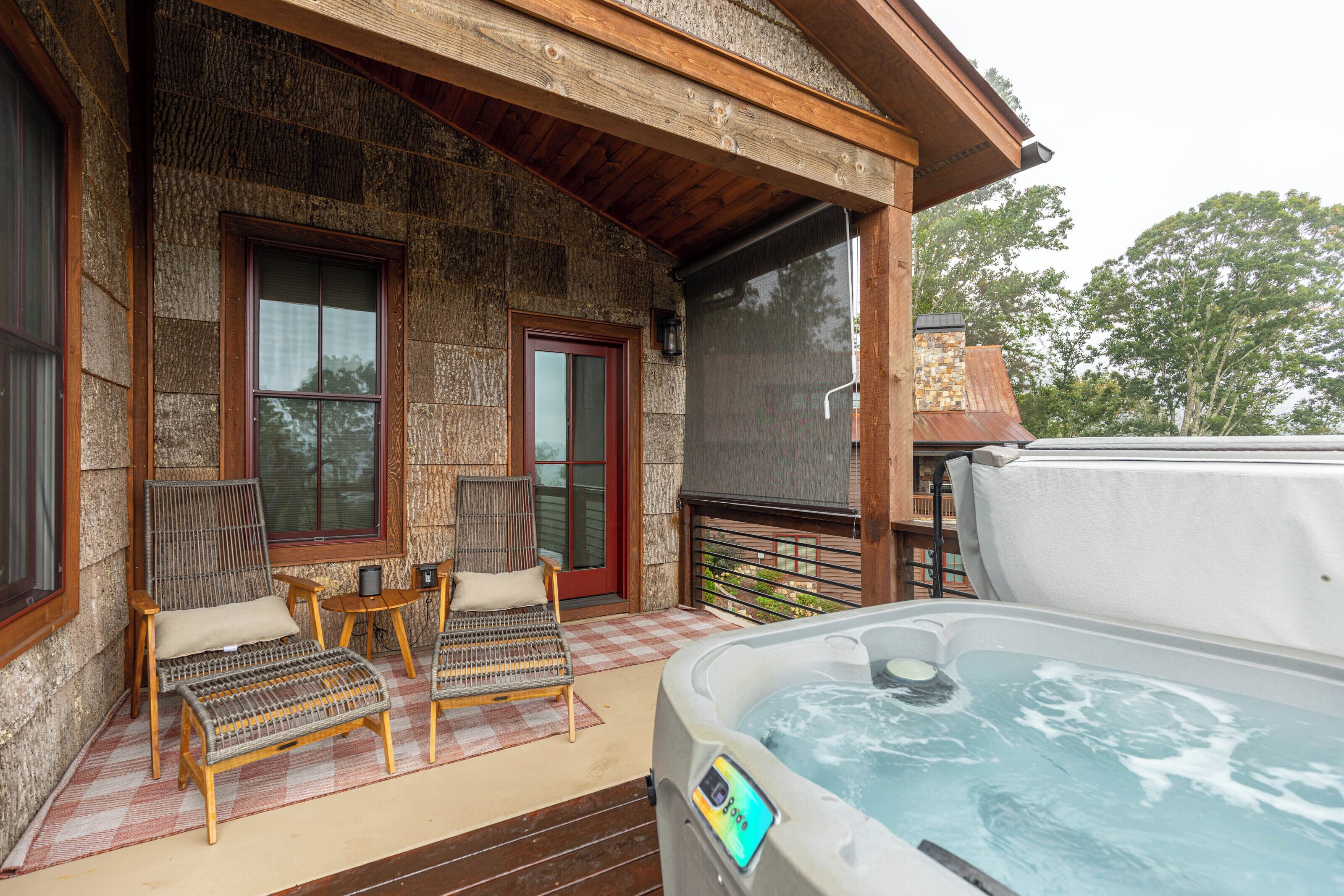 A stone building with a screened porch, two wicker chairs, a small table, and a hot tub.