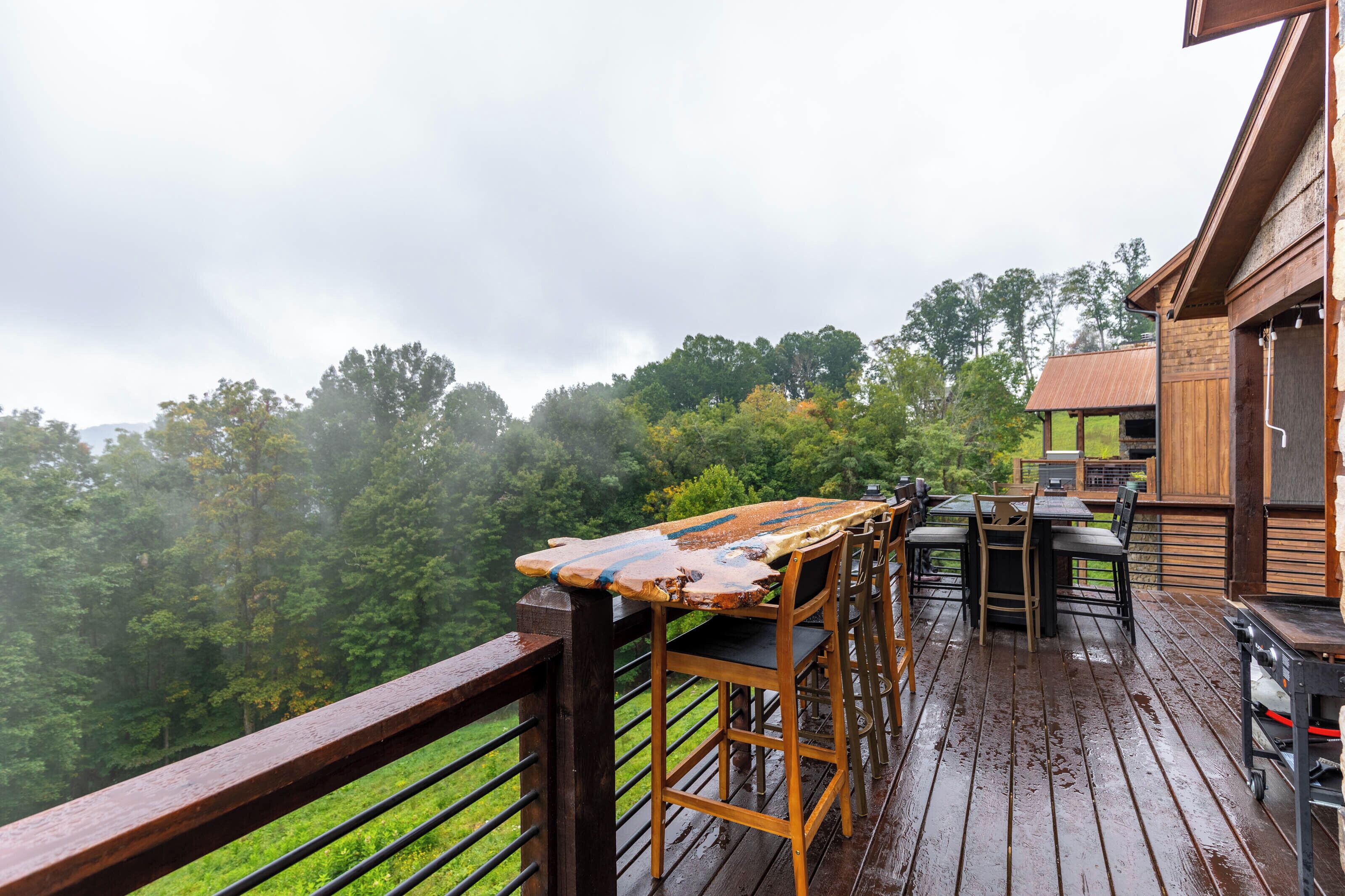 A wooden deck with a table and chairs, overlooking a forested area.