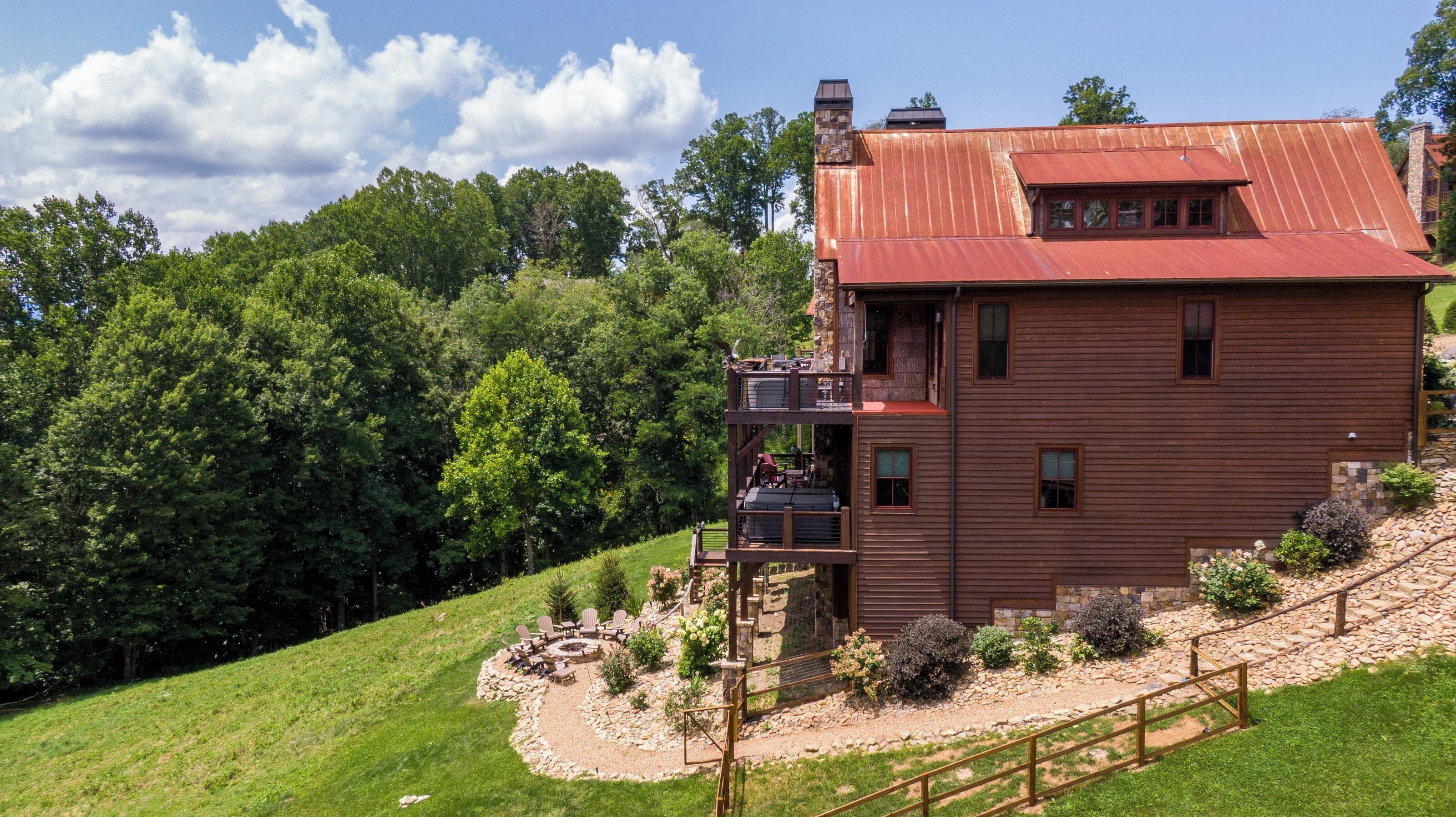 A two-story wooden cabin with a red roof, a balcony, and a stone foundation.