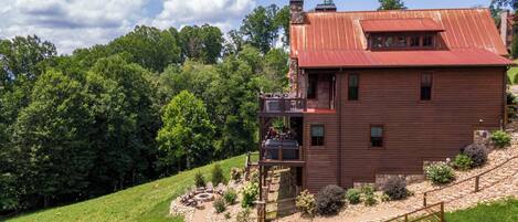 A two-story wooden cabin with a red roof, a balcony, and a stone foundation.