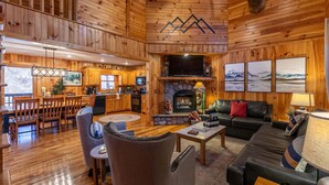 A log cabin interior with a dining area, kitchen, fireplace, and living room. - Riverbend Retreat (Todd)