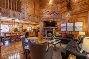 A log cabin interior with a dining area, kitchen, fireplace, and living room. - Riverbend Retreat (Todd)
