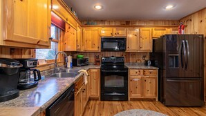 A kitchen with wooden cabinets, a microwave, a stove, a refrigerator, and a coffee maker. - Riverbend Retreat (Todd)