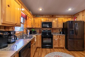 A kitchen with wooden cabinets, a microwave, a stove, a refrigerator, and a coffee maker. - Riverbend Retreat (Todd)