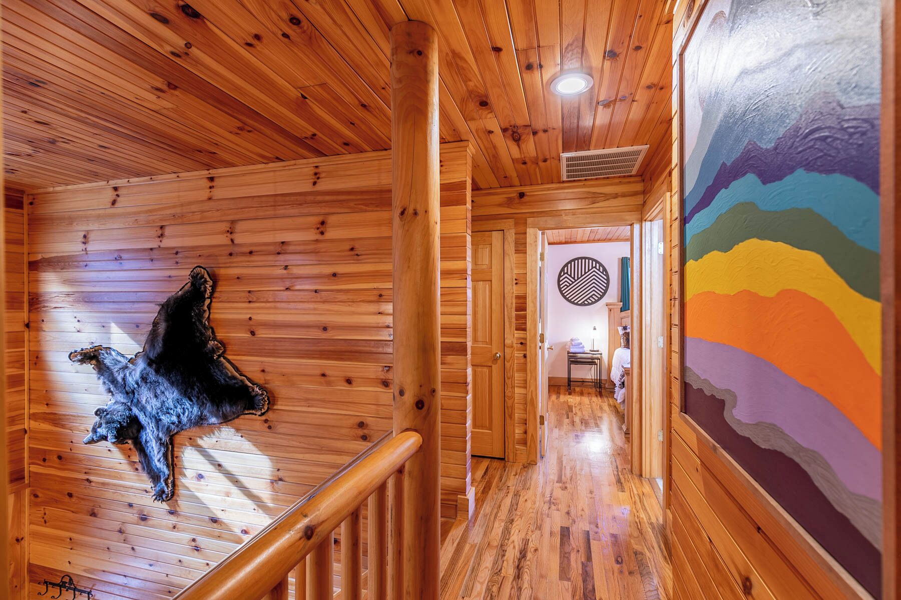 A wooden interior with a bear sculpture, a colorful mural, and a hallway leading to a room with a circular patterned wall.