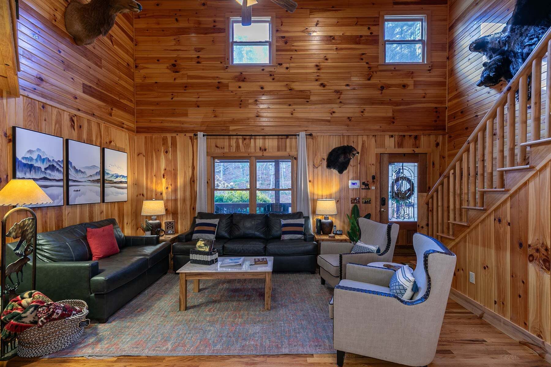 A cozy cabin interior with a wooden interior, a sofa, a chair, a coffee table, and a staircase.