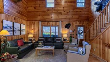 A cozy cabin interior with a wooden interior, a sofa, a chair, a coffee table, and a staircase.