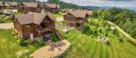 A cluster of wooden cabins with balconies, surrounded by a well-maintained lawn and a view of a forested mountain range.