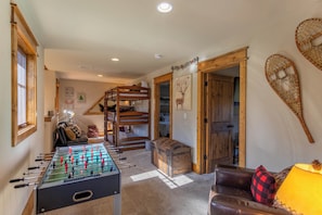 Une pièce chaleureuse avec une table de baby-foot, un lit superposé, un canapé en cuir et une malle en bois.