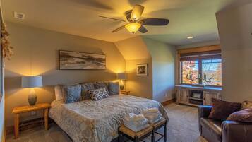 A bedroom with a large bed, two bedside lamps, a ceiling fan, a window with a view, and a bench with towels.