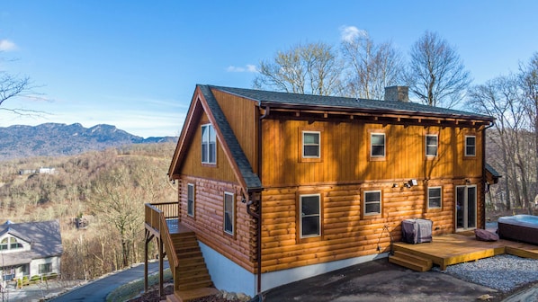 A log cabin with a deck, a hot tub, and a scenic mountain view.