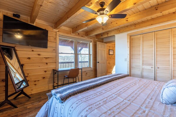Ein Zimmer in einer Holzhütte mit einem Bett, einem Deckenventilator, einem Fernseher, einem Fenster und einer Tür.