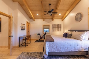 A bedroom with a bed, a desk, an exercise bike, and a ceiling fan. - Ursa Minor (Banner Elk)