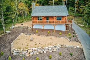 Eine Holzhütte mit Balkon, umgeben von einem angelegten Garten mit Steinmauer und kleinen Bäumen.