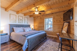 Un dormitorio de cabaña de madera con una cama, una mesa y un ventilador de techo.