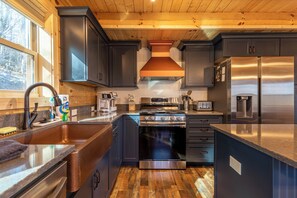 A modern kitchen with dark cabinets, stainless steel appliances, and a large window.