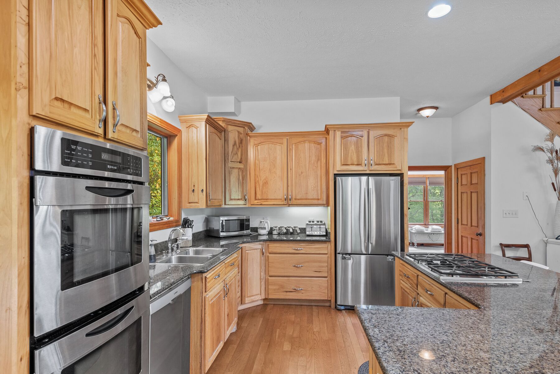 A kitchen with wooden cabinets, stainless steel appliances, granite countertops, and a view to the outside.