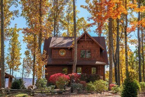 Eine Hütte, umgeben von hohen Bäumen im Herbstlaub.