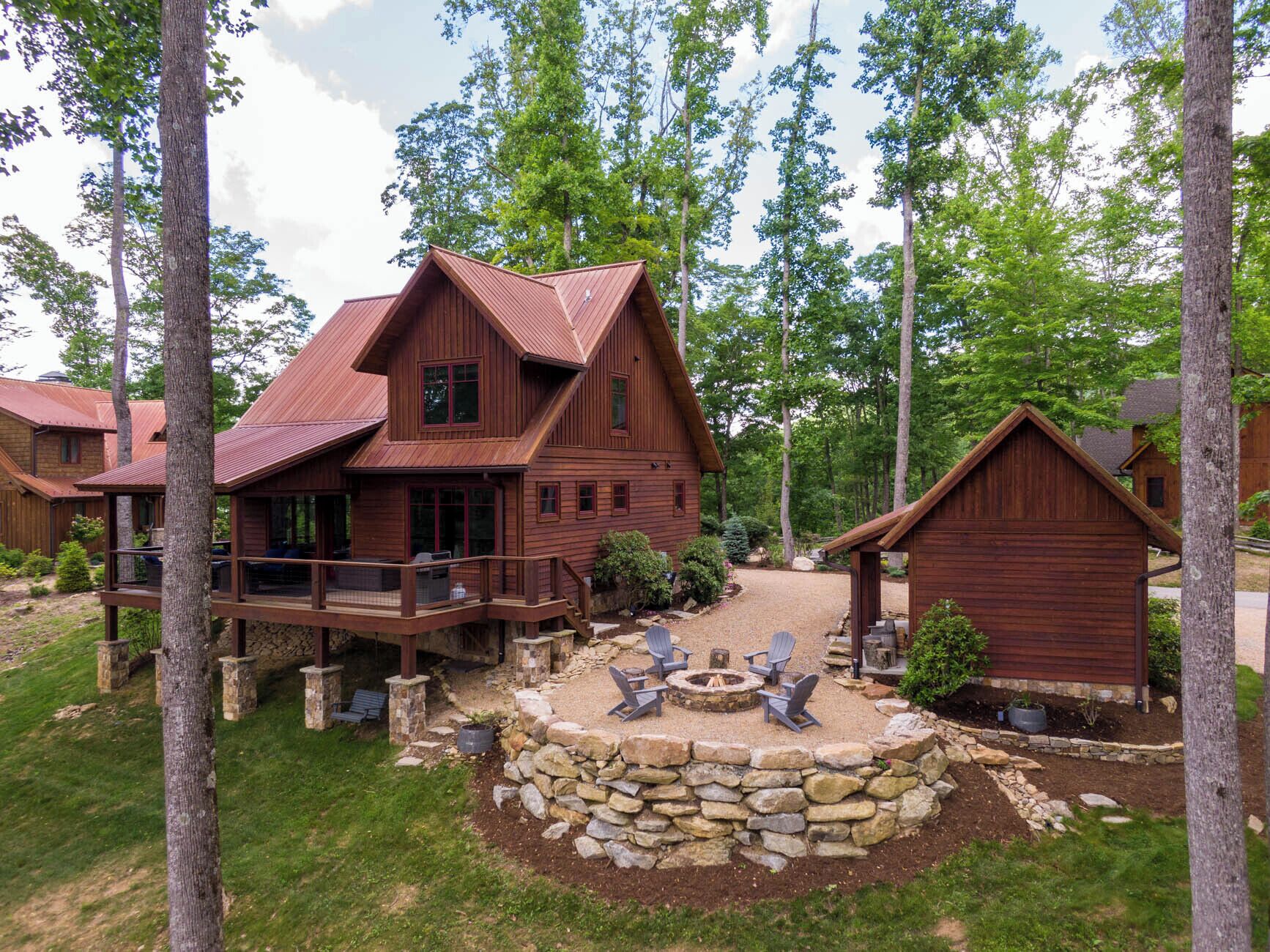 A wooden cabin with a deck, a fire pit, and a stone wall.