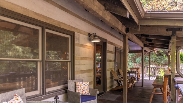A covered outdoor seating area with wicker furniture, large windows, and a wooden deck. - Blackberry Creek Cabin (Lenoir)