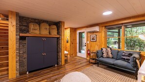 A cozy room with a stone wall, wooden beams, a dark blue cabinet, a gray sofa, and a window with a view of greenery. - Blackberry Creek Cabin (Lenoir)