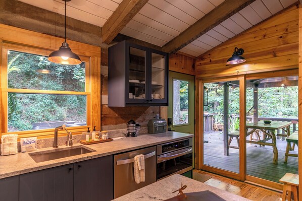 A kitchen with a built-in oven, a sink, and a window overlooking a deck.