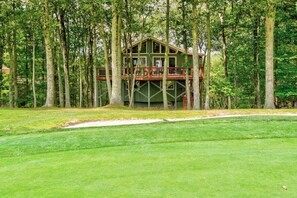 A two-story wooden cabin with a deck, surrounded by tall trees and a well-maintained lawn. - Love to Beech - Beech Mtn on Golf Course, hot Tub, Pool Table, Club Access Options (Banner Elk)