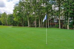 A well-maintained golf course with a flagstick in the foreground, surrounded by lush greenery and tall trees. - Love to Beech - Beech Mtn on Golf Course, hot Tub, Pool Table, Club Access Options (Banner Elk)