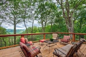 Eine Holzterrasse mit Gartenmöbeln, darunter Stühle und ein Tisch, umgeben von Bäumen und einer schönen Aussicht.