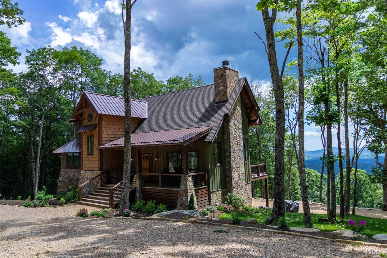 A cabin with a stone chimney, wooden exterior, and a porch with steps leading to a door.